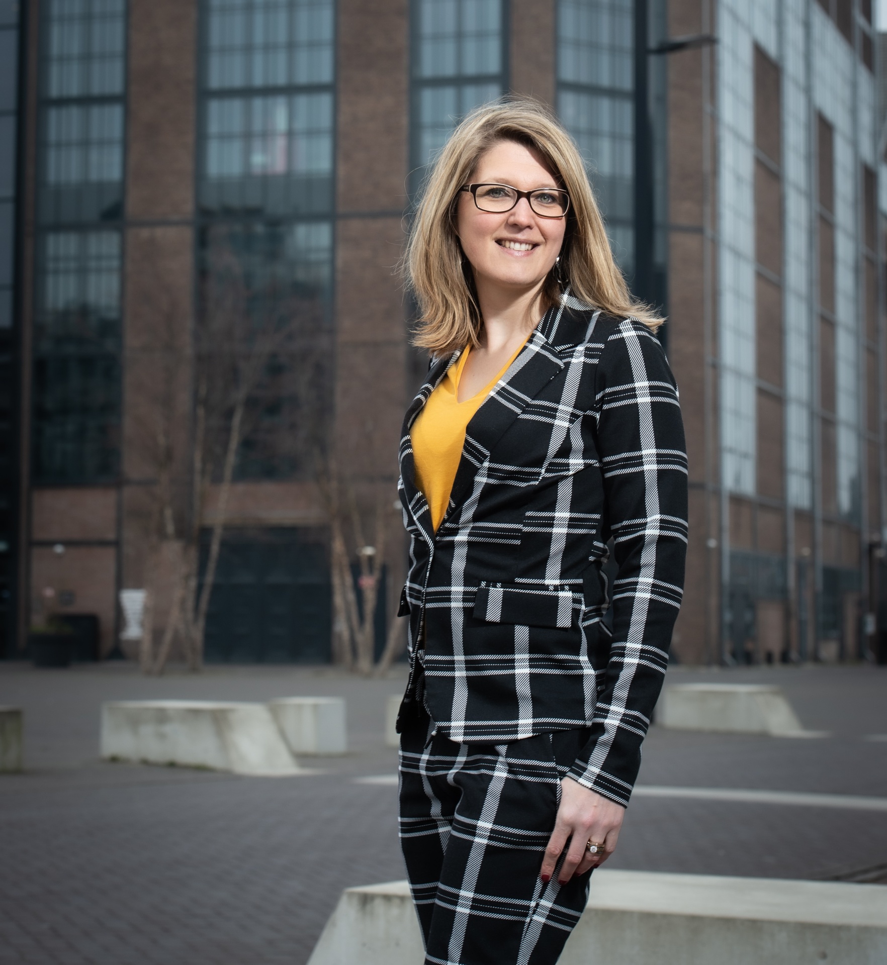 Portret van Diana Langerak in een geruit pak voor een modern gebouw